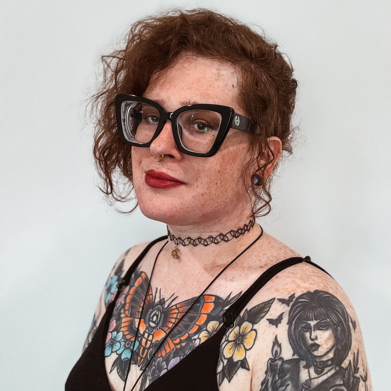 a photo of parker lee from the waist up. she is wearing a black scoop neck dress and a black cord necklace with a piece of sodalite hanging from it. parker's left arm as at her hip, and her head is tilted slightly to the right of the photo.